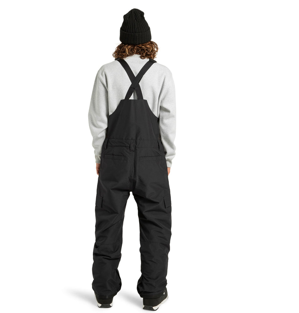 A person wearing a black beanie, a light gray sweatshirt, and the DC Shoes Men’s Docile Bib Insulated Bib stands facing away from the camera against a plain white background.