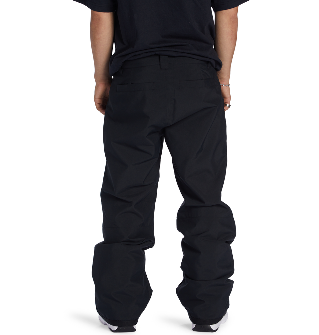 A person is shown from the waist down, wearing loose black DC Shoes Men’s Insulated Chino Pants and a black t-shirt, standing with their back to the camera against a plain white background.