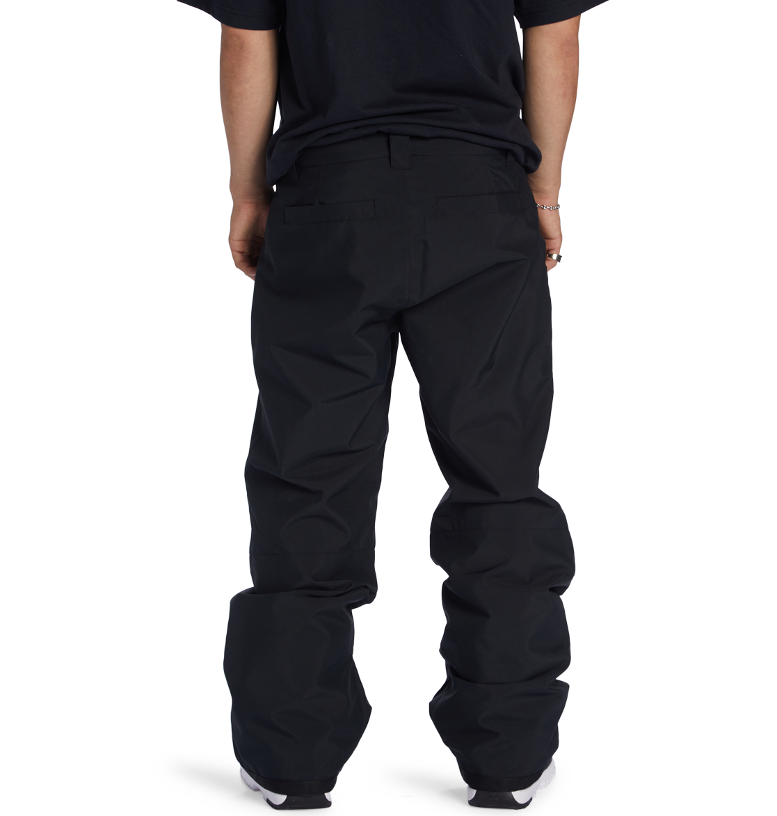 A person is shown from the waist down, wearing loose black DC Shoes Men’s Insulated Chino Pants and a black t-shirt, standing with their back to the camera against a plain white background.