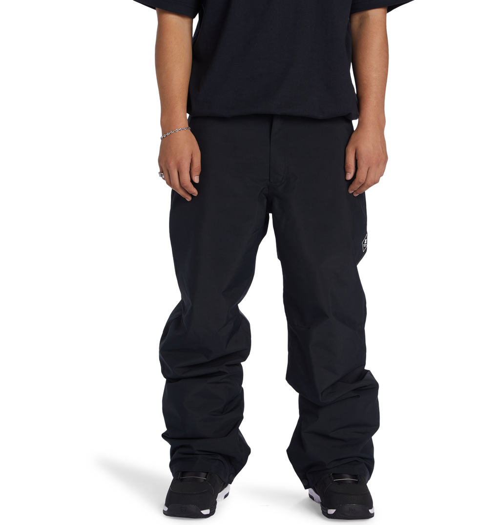 A person stands facing forward against a plain white background, wearing DC Shoes Men’s Insulated Chino Pants, a black T-shirt, black shoes, and a silver bracelet. Their face is not visible.