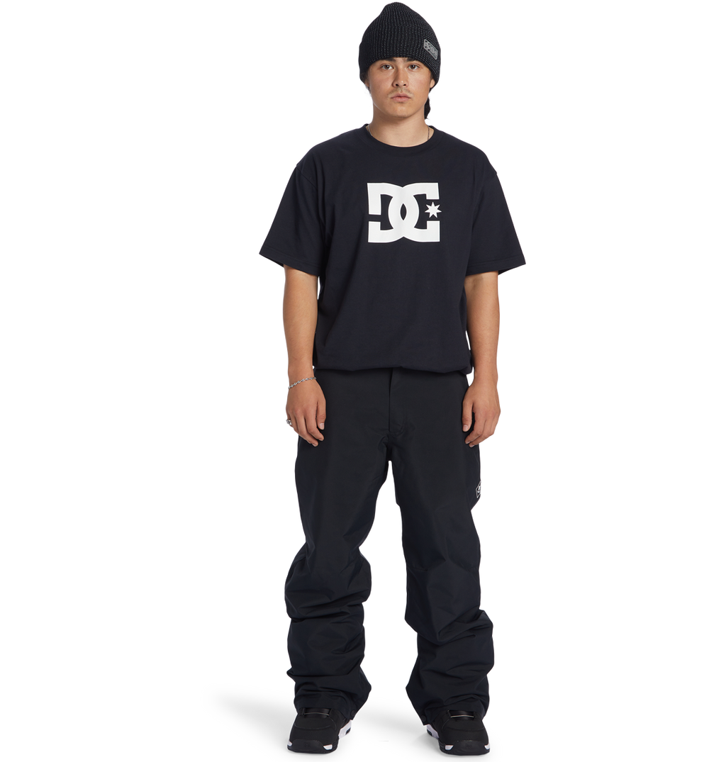 A person wearing a black beanie, black DC Shoes t-shirt, Men’s Insulated Chino Pants by DC Shoes, and black shoes stands facing forward against a white background.