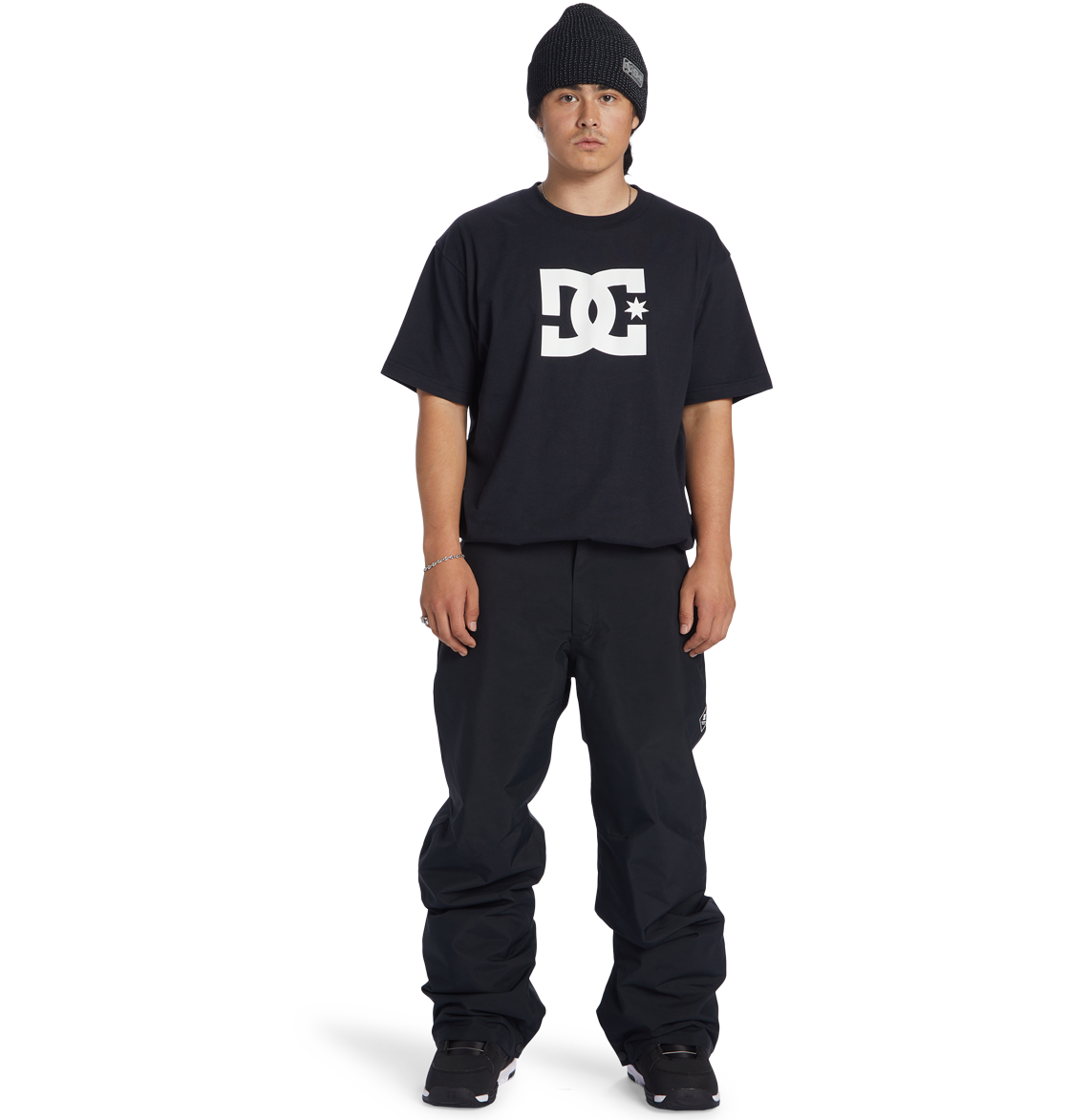 A person wearing a black beanie, black DC Shoes t-shirt, Men’s Insulated Chino Pants by DC Shoes, and black shoes stands facing forward against a white background.