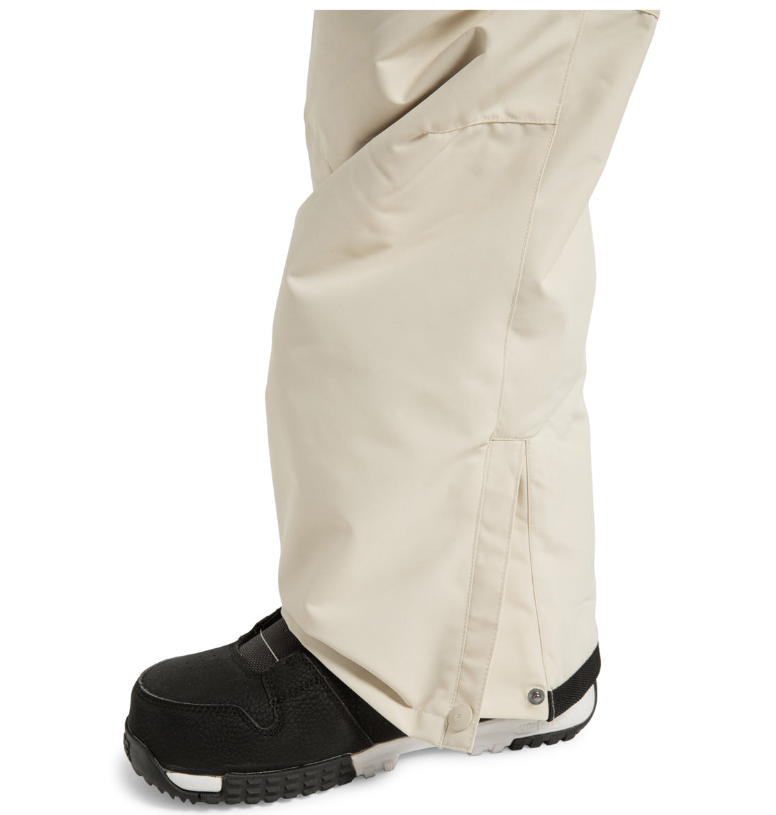 A close-up of a person wearing DC Shoes Men’s Insulated Chino Pants made from recycled polyester over black snow boots, with the pants covering most of the boots and secured with a snap closure near the ankle for enhanced weather protection.