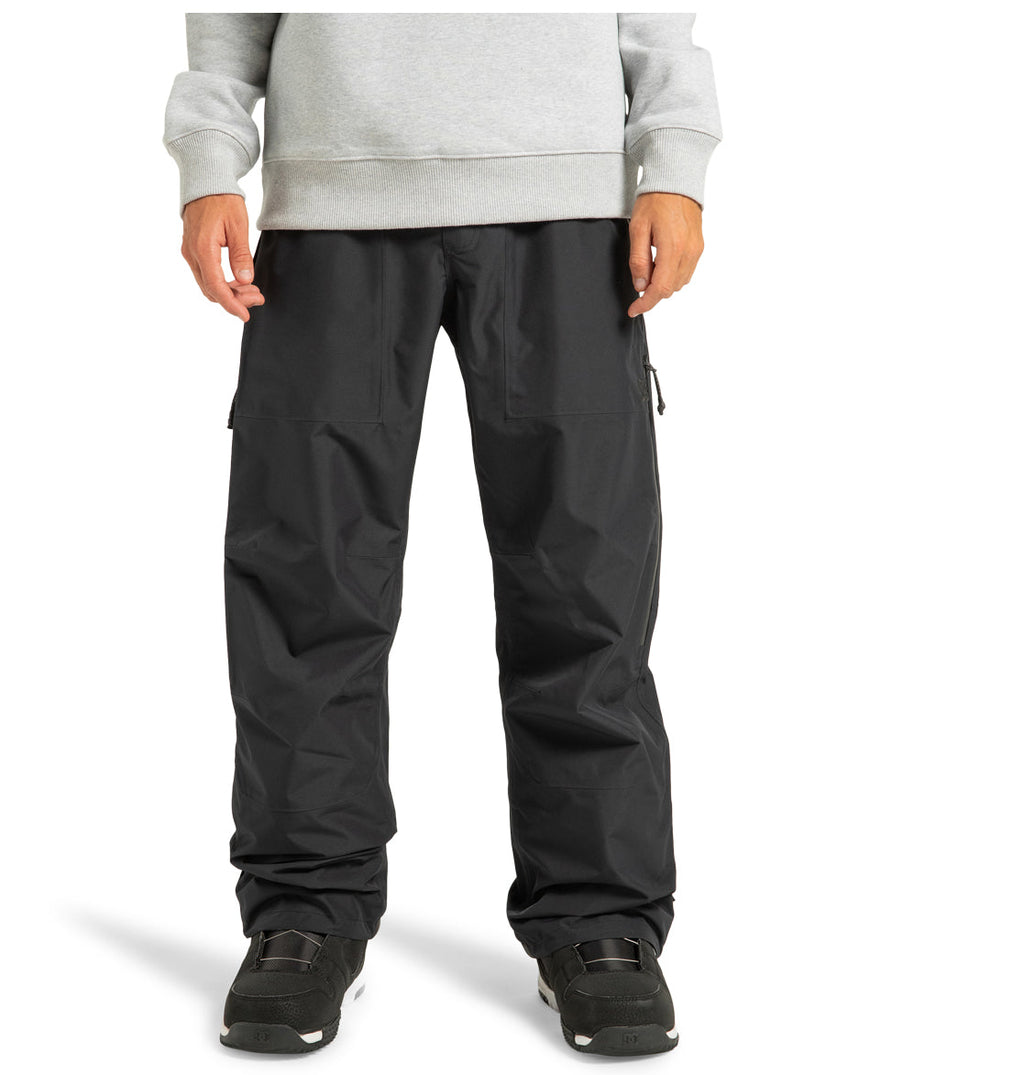 A person is shown from the waist down, wearing black Unisex Squadron 30K Insulated Pants by DC Shoes, paired with black shoes and a light gray sweatshirt, standing against a white background. The cropped image focuses on the lower half of the body—perfectly showcasing these insulated pants built by DC Shoes for dependable weather protection during any winter adventure.