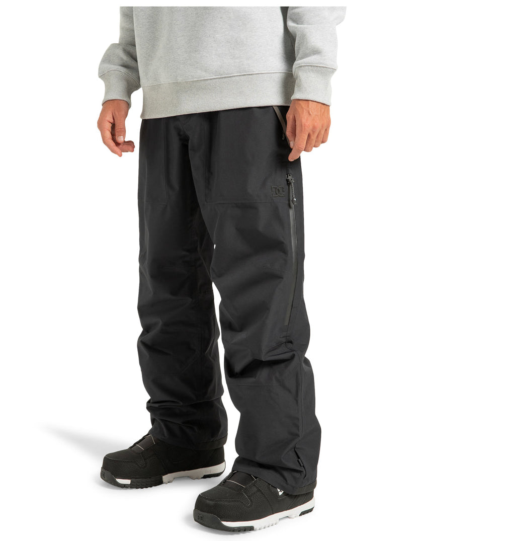 A person wearing a light gray sweatshirt, DC Shoes’ Unisex Squadron 30K Insulated Pants featuring a zippered pocket, and black winter boots stands against a plain white background—ready for any winter adventure.