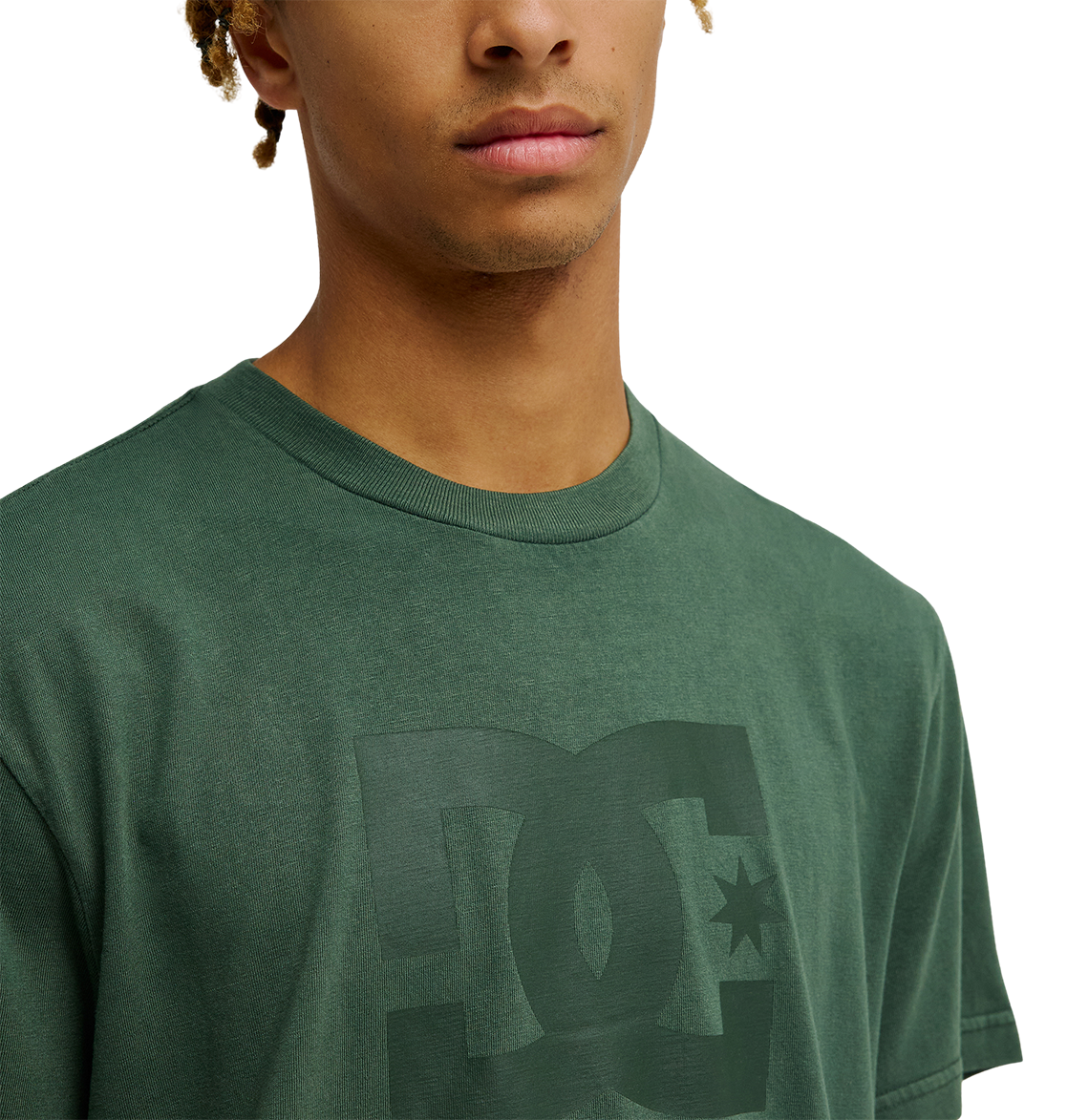 A person is shown from the shoulders up against a plain background, wearing the Men's DC Star Pigment Dye Tee by DC Shoes—a green skate t-shirt featuring a subtle logo on the front and a relaxed fit.