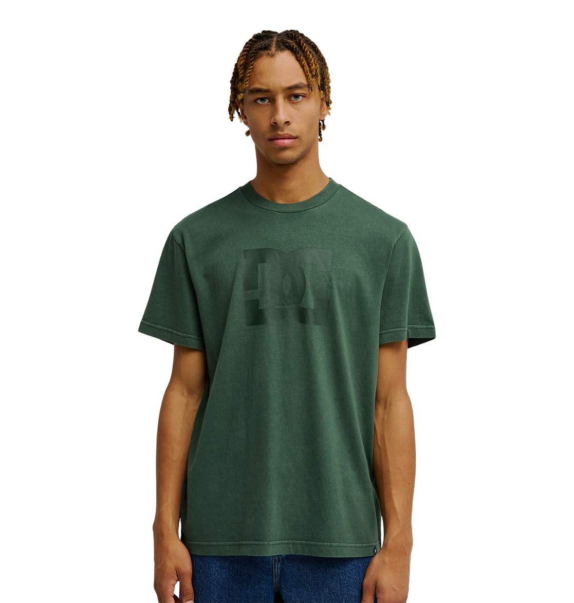 A person with short, curly hair is wearing the Men's DC Star Pigment Dye Tee by DC Shoes—a dark green graphic skate shirt featuring a subtle DC artwork design and a relaxed fit—while standing against a plain white background.