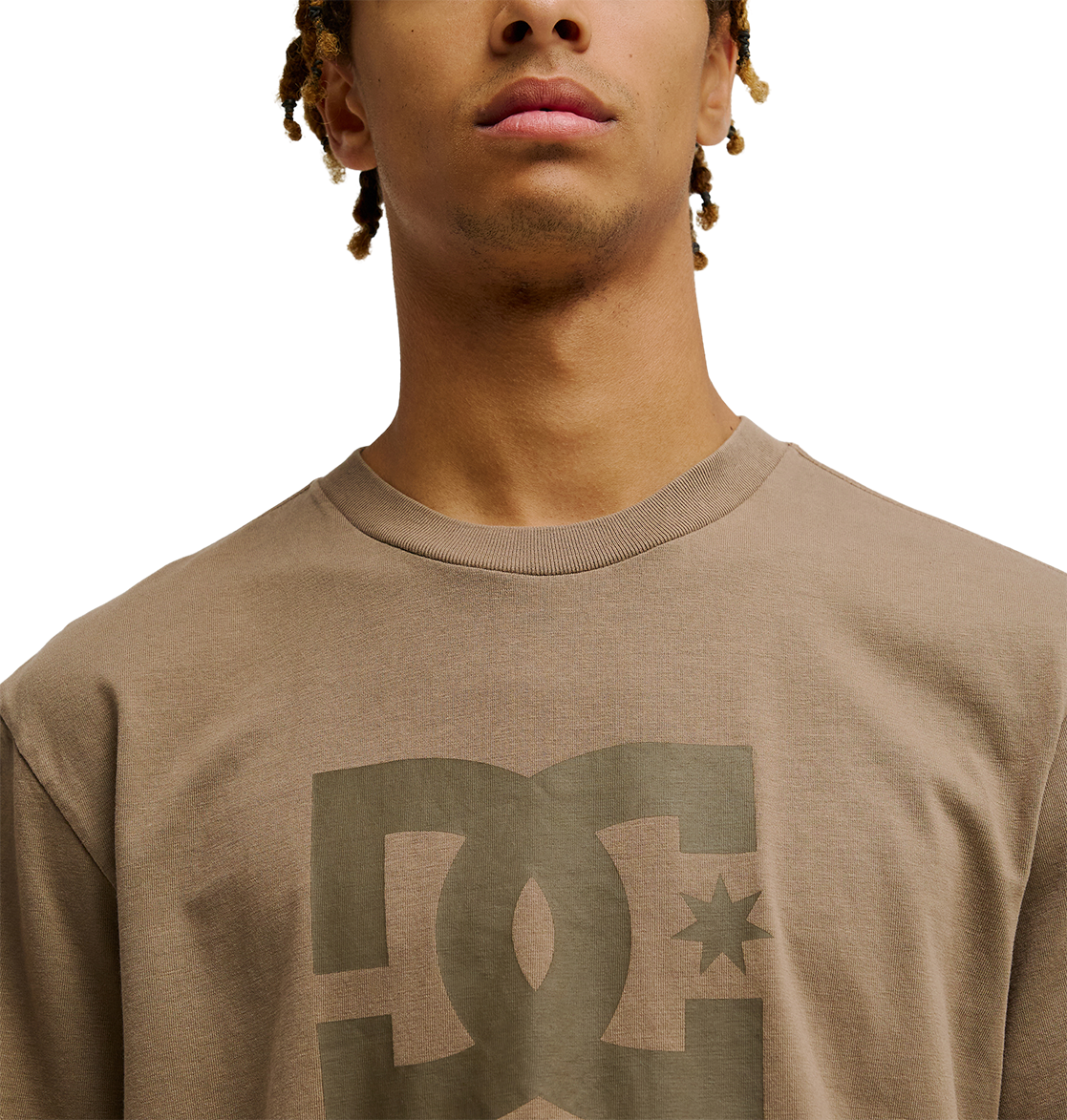 A young person wearing the Men's DC Star Pigment Dye Tee by DC Shoes in taupe, featuring the DC logo, shown from the shoulders up with a neutral expression against a plain white background.