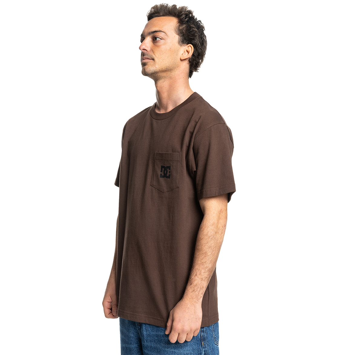 A man stands sideways against a white background, wearing the Men's DC Star Pocket Tee by DC Shoes—a relaxed fit brown skate shirt with a chest pocket and small logo—paired with blue jeans.