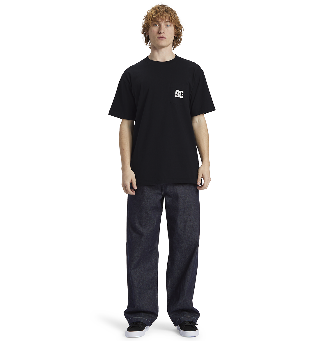 A person with curly hair wears the Men's DC Star Pocket Tee by DC Shoes in black, paired with relaxed fit dark jeans and black shoes, standing against a plain white background.