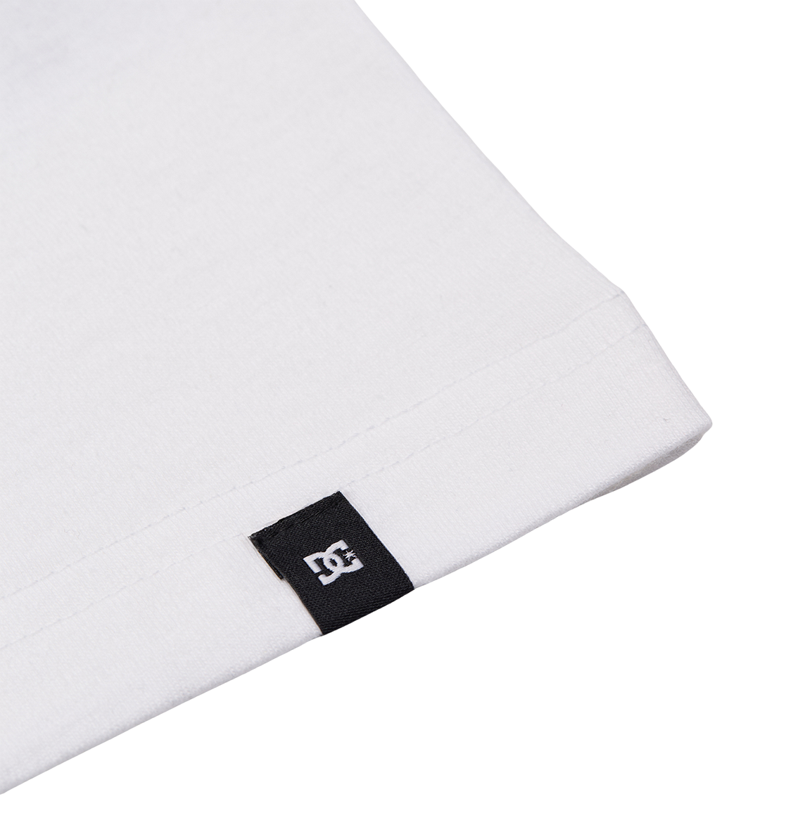 Close-up of the hem on the Men's DC Corpo Tee by DC Shoes, showing a small black fabric tag with the white DC Shoes logo stitched to the edge.