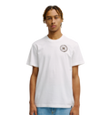A young man with short, braided hair models the Men's DC Corpo Tee by DC Shoes—a relaxed fit, plain white t-shirt with a small black DC logo and circular emblem on the left chest—paired with light blue jeans against a white background.
