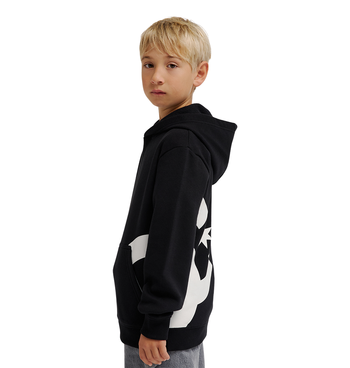 A young boy with blond hair wears the DC Shoes Lanai Hoodie Youth, a black pullover with bold side graphics, standing sideways and looking at the camera against a plain white background.