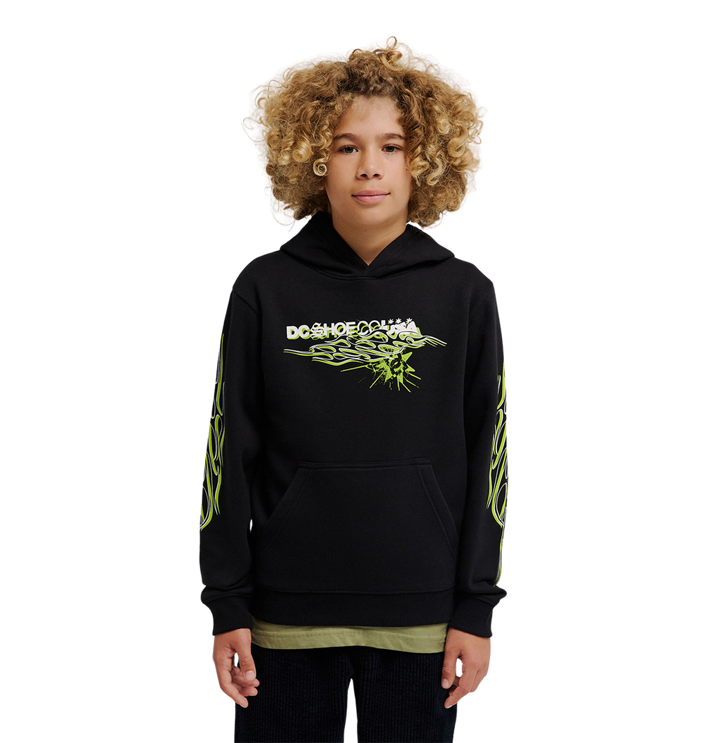 A young person with curly hair wears the DC Shoes Side Flame Hoodie Youth, a black pullover featuring neon green designs and a bold DC Shoes logo, standing against a plain white background.