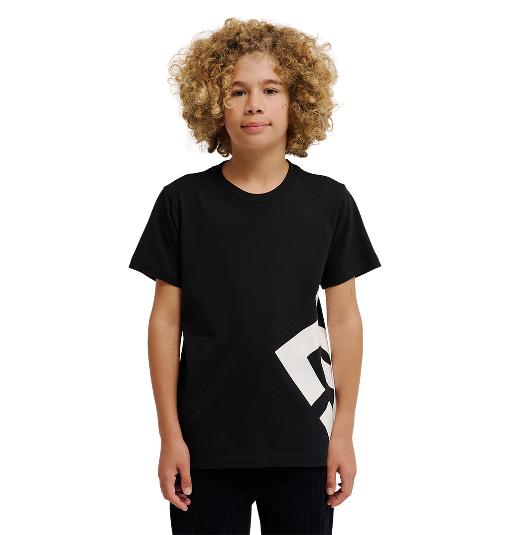 A young person with curly blonde hair wears the DC Shoes DC Lanai Tee Youth, a black relaxed-fit skate shirt with a bold white graphic on one side, standing against a plain white background.