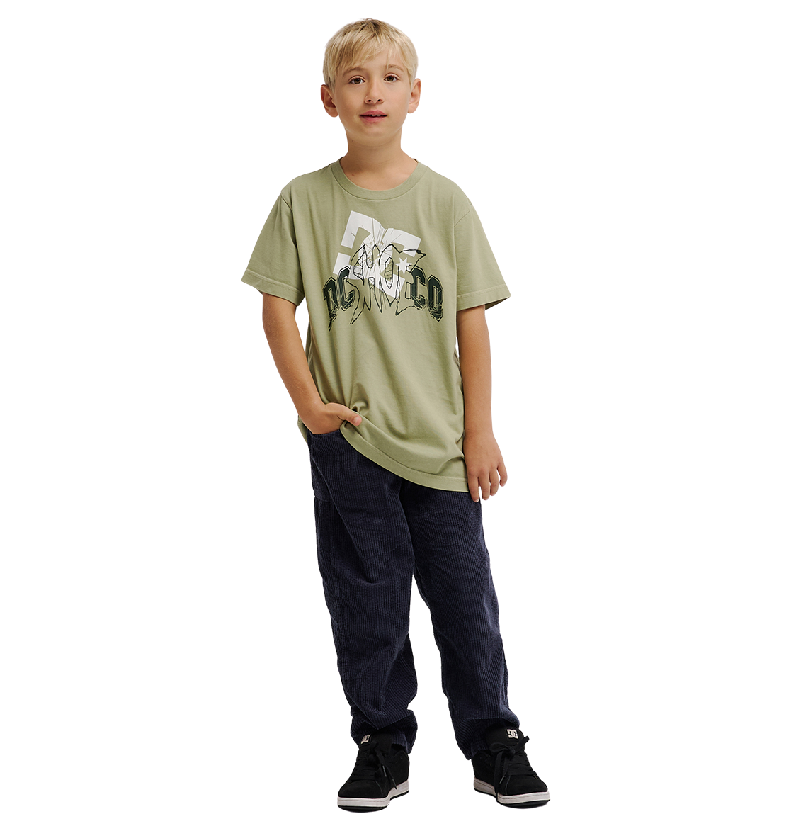 A blonde boy stands with one hand in his pocket against a plain white background, wearing the DC Shoes DC Speratic Tee Youth—a light green, heritage-inspired graphic skate t-shirt in a relaxed fit—paired with dark pants and black sneakers.