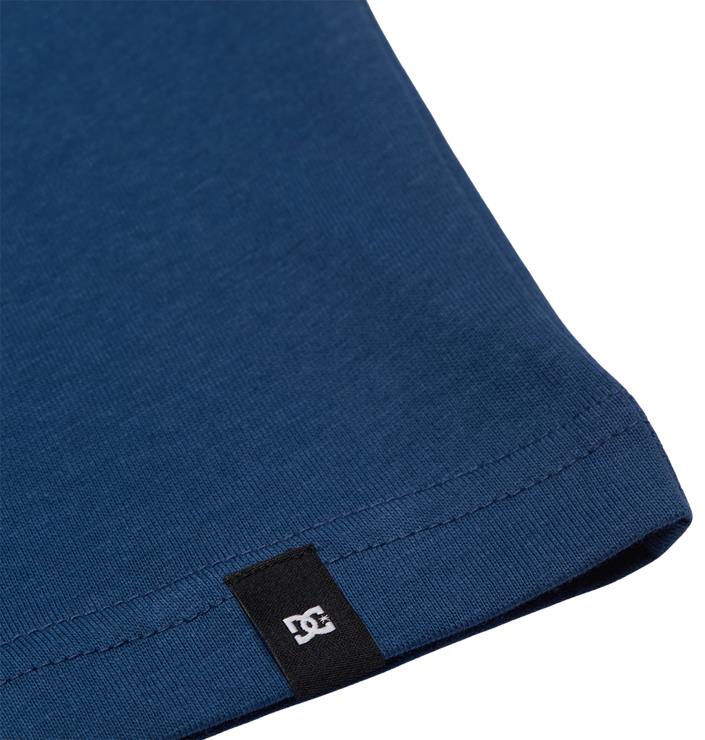 Close-up of the hem of the blue DC Star Filled Tee Youth by DC Shoes, featuring a small black tag with a white logo near the edge.