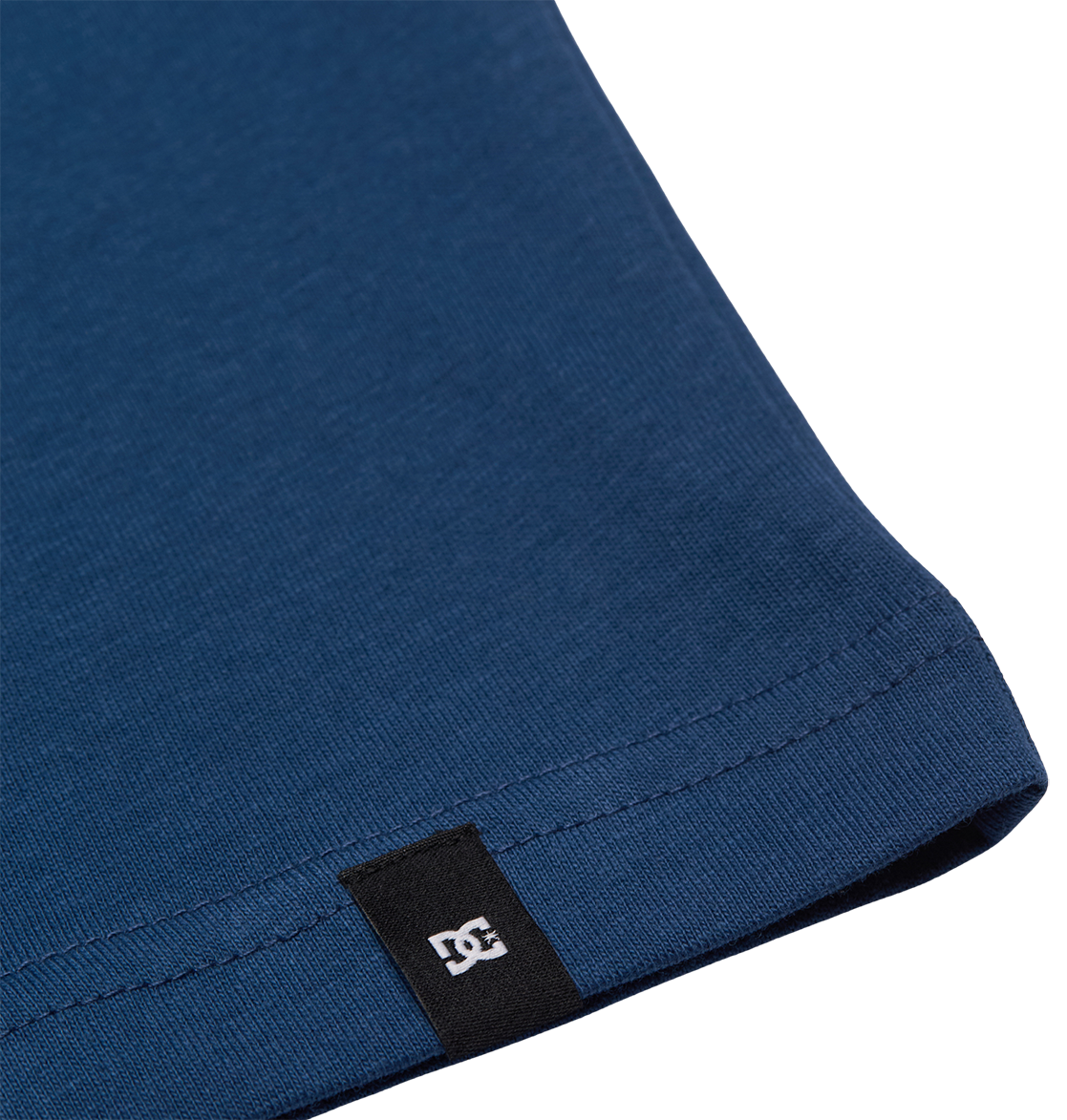 Close-up of the hem of the blue DC Star Filled Tee Youth by DC Shoes, featuring a small black tag with a white logo near the edge.
