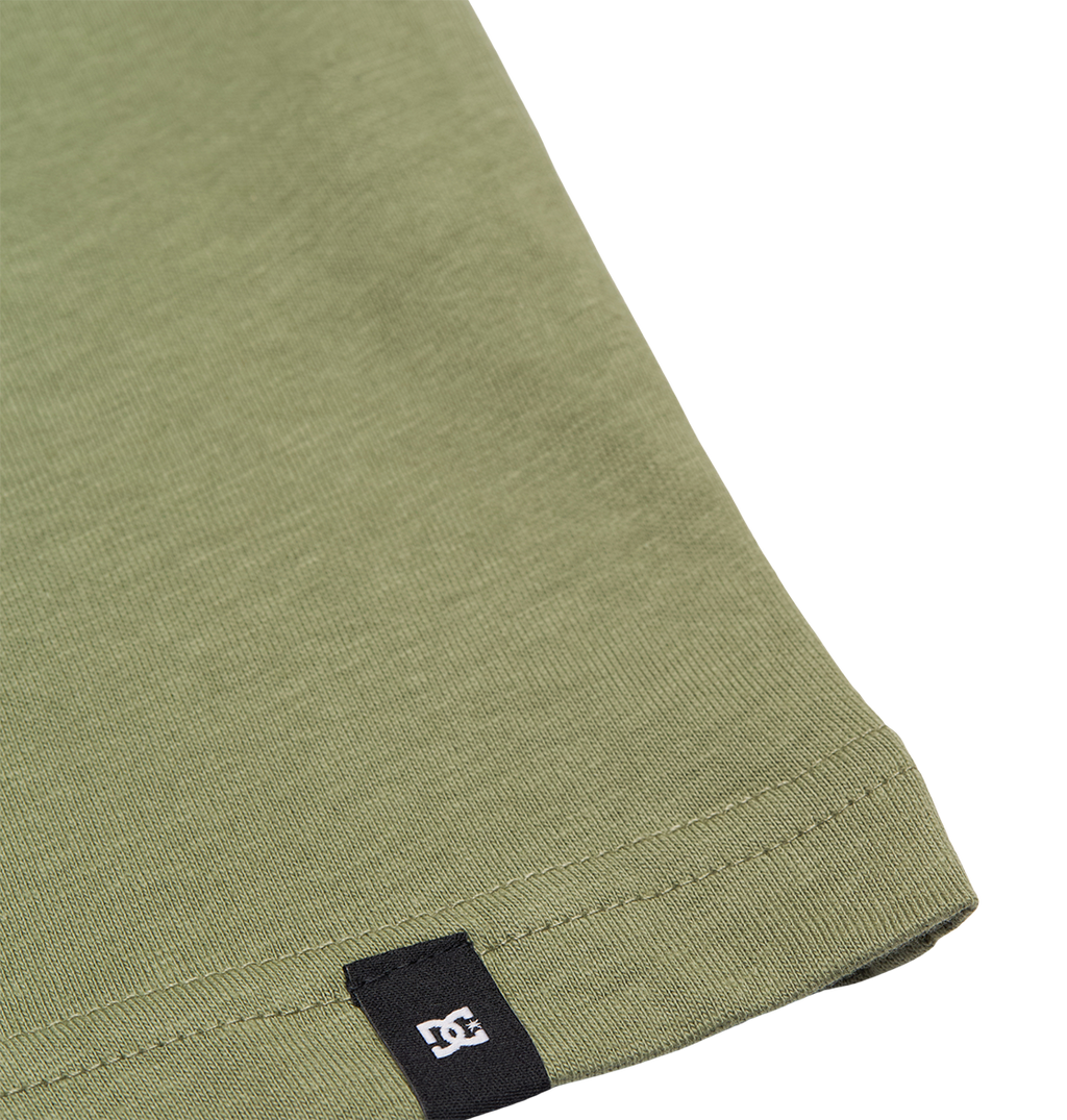 Close-up of the hem of the DC Shoes DC Star Filled Tee Youth in olive green, a relaxed fit t-shirt, featuring a small black tag with a white logo near the edge.