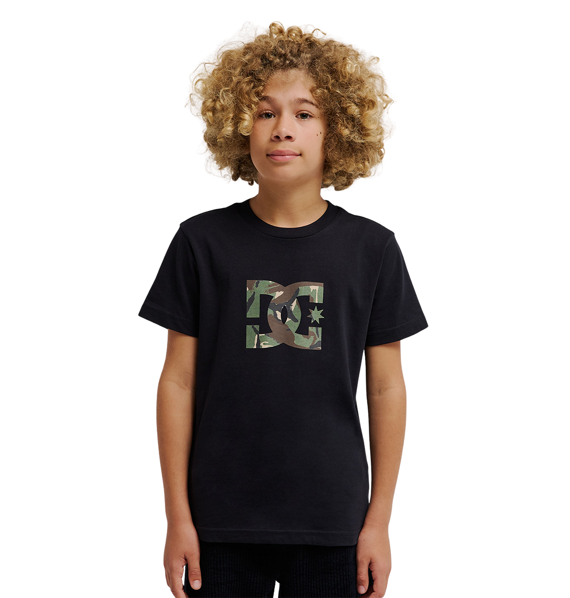 A young person with curly blond hair wears the DC Shoes DC Star Filled Tee Youth, a relaxed fit black graphic skate T-shirt featuring a camo-print DC Shoes star artwork logo on the chest, standing against a plain white background.
