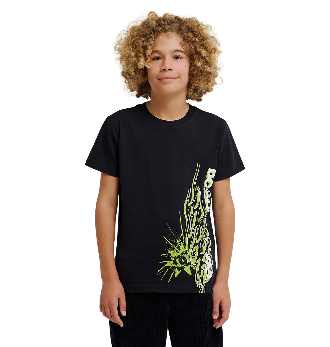 A young person with curly blond hair wears the DC Shoes DC Side Flame Tee Youth, a relaxed fit black skate t-shirt featuring a neon green and white abstract design on the lower side, standing against a plain white background.