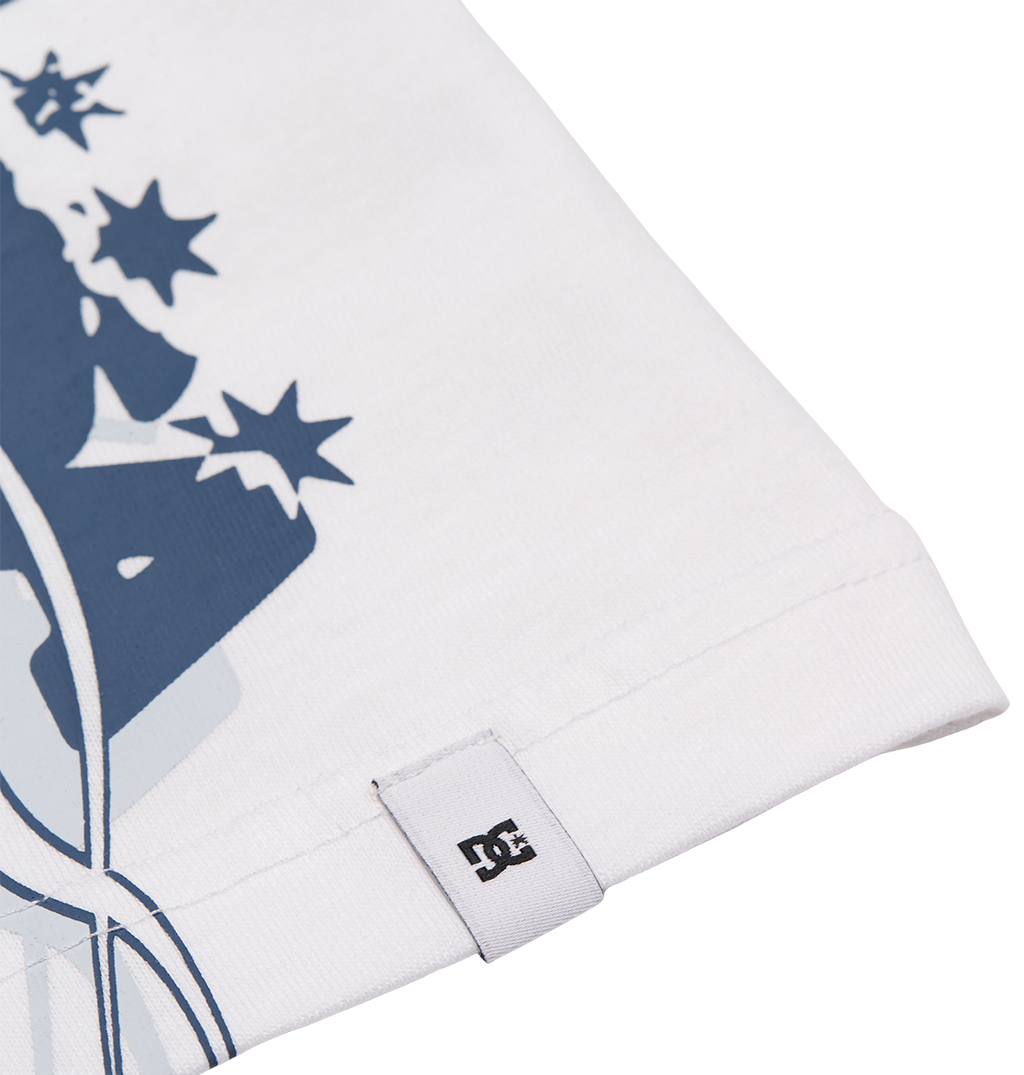 Close-up of the hem on the DC Shoes Side Flame Tee Youth in white, featuring a small DC logo tag. A section of the tee’s bold blue graphic with stars is visible, reflecting its relaxed fit and skate-inspired style.