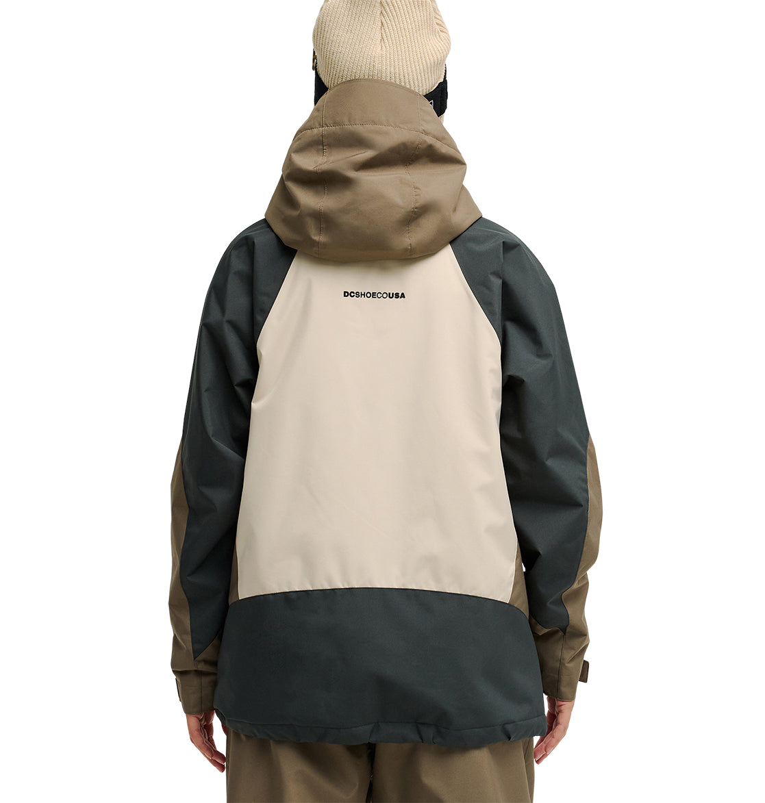 A person seen from the back wearing the DC Shoes Everfrost Jacket—a tan and dark green hooded waterproof jacket with “DC SHOES CO USA” printed on the upper back—paired with a beige beanie.