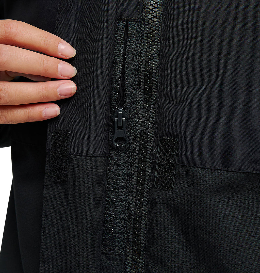 A close-up of a hand touching the chest area of the black DC Shoes Cruiser Jacket, highlighting the zipper and small Velcro patches.