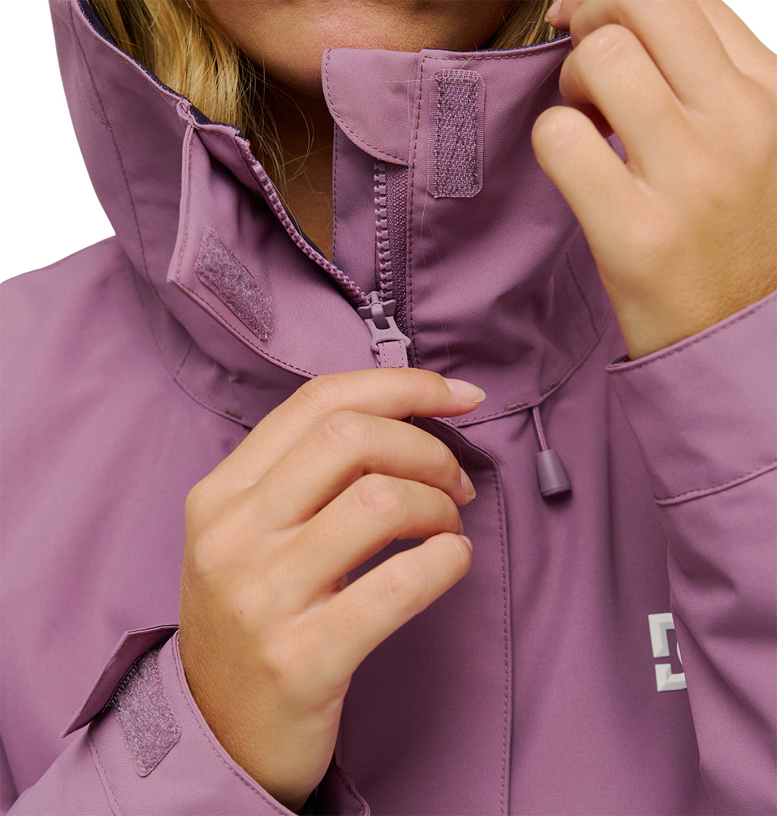 A person wearing the DC Shoes Cruiser Jacket in lavender is zipping it up. The image highlights their hands and the jacket, showcasing details such as velcro straps and a white DC Shoes logo on the chest.