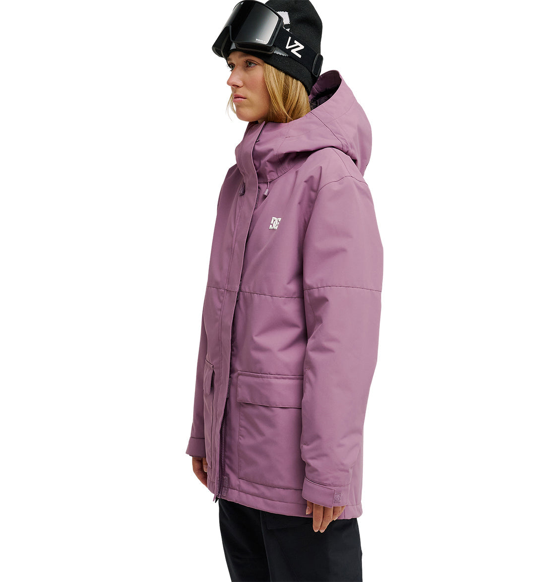 A person wearing a purple DC Shoes Cruiser Jacket, black ski goggles, and a black beanie stands facing left against a white background.
