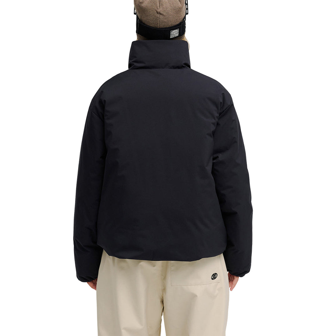 A person is facing away, wearing the DC Shoes Aura Puffer Jacket in black, paired with beige pants and a beige beanie. The plain white background highlights the outfit from the back.