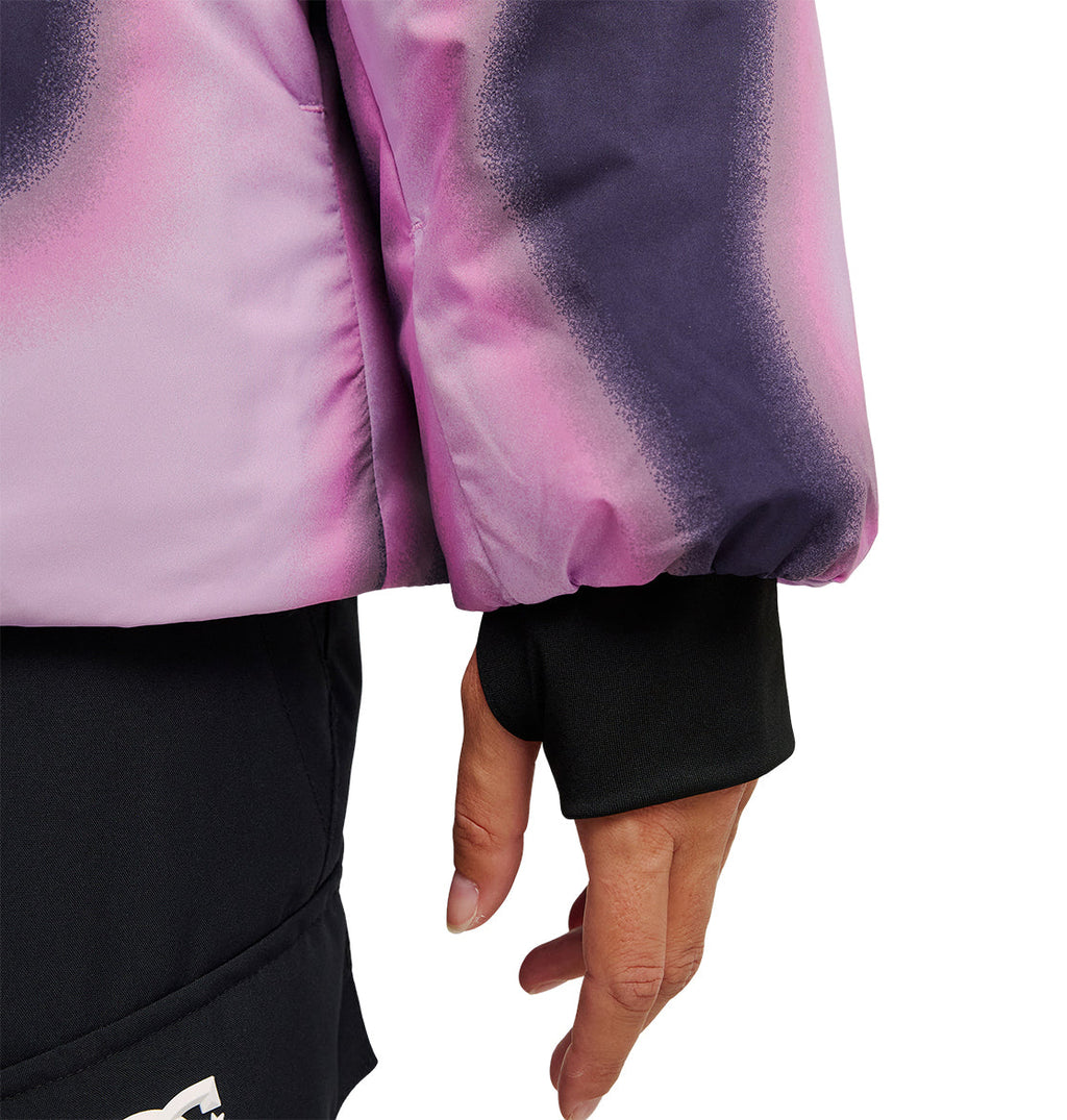 A person’s hand hangs at their side, the black sleeve with a thumb hole peeking out from beneath the DC Shoes Aura Puffer Jacket in pink and purple—a waterproof piece designed for snow performance. The jacket meets black pants, which feature a small white logo near the hem.