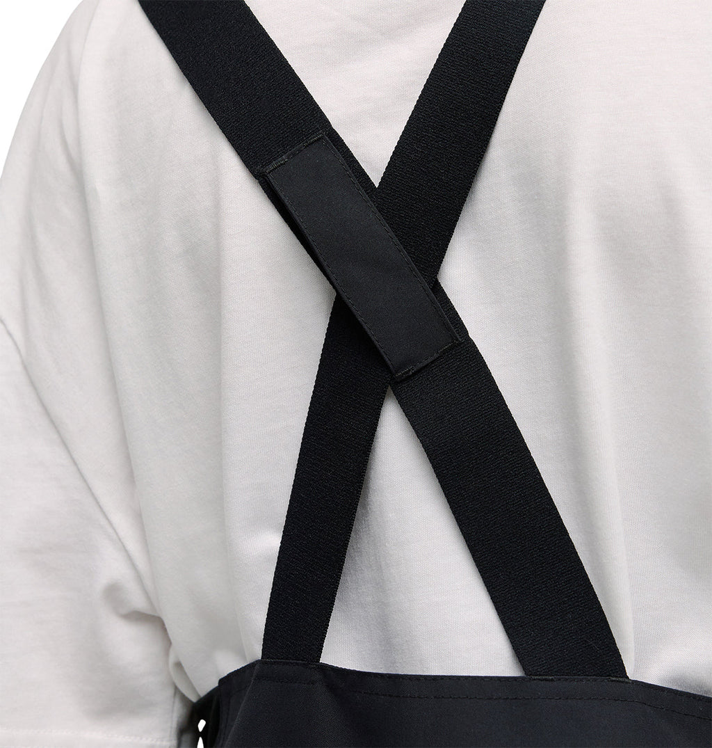 A close-up of a person wearing the DC Shoes Valiant Bib Pants, featuring crossed straps on their back and designed for breathable protection during any task.