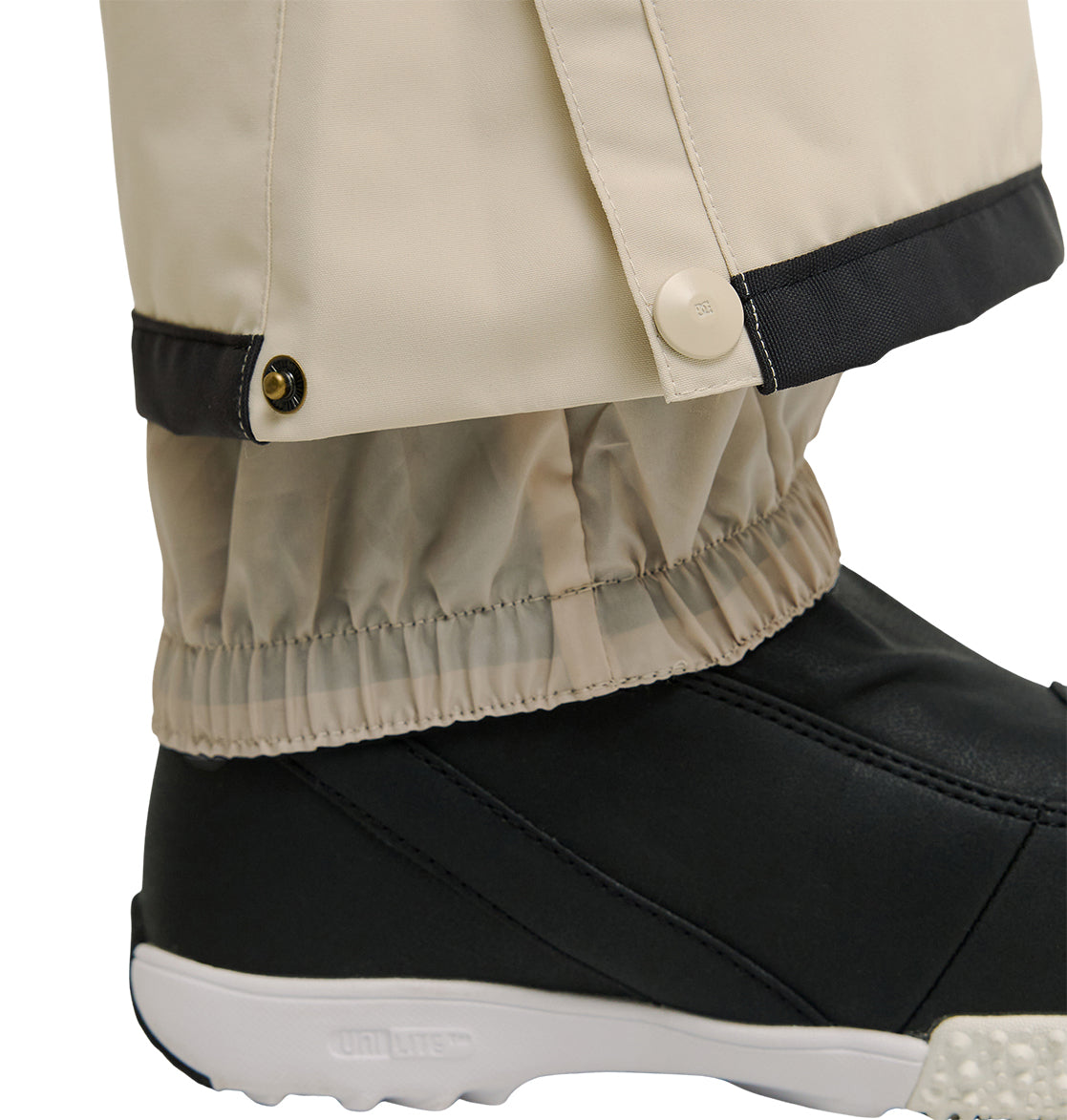Close-up of the Nonchalant Pants by DC Shoes in beige, showcasing a buttoned cuff over a black shoe. These insulated snow pants feature an elastic inner gaiter that fits snugly around the ankle above the shoe, delivering added warmth and protection.