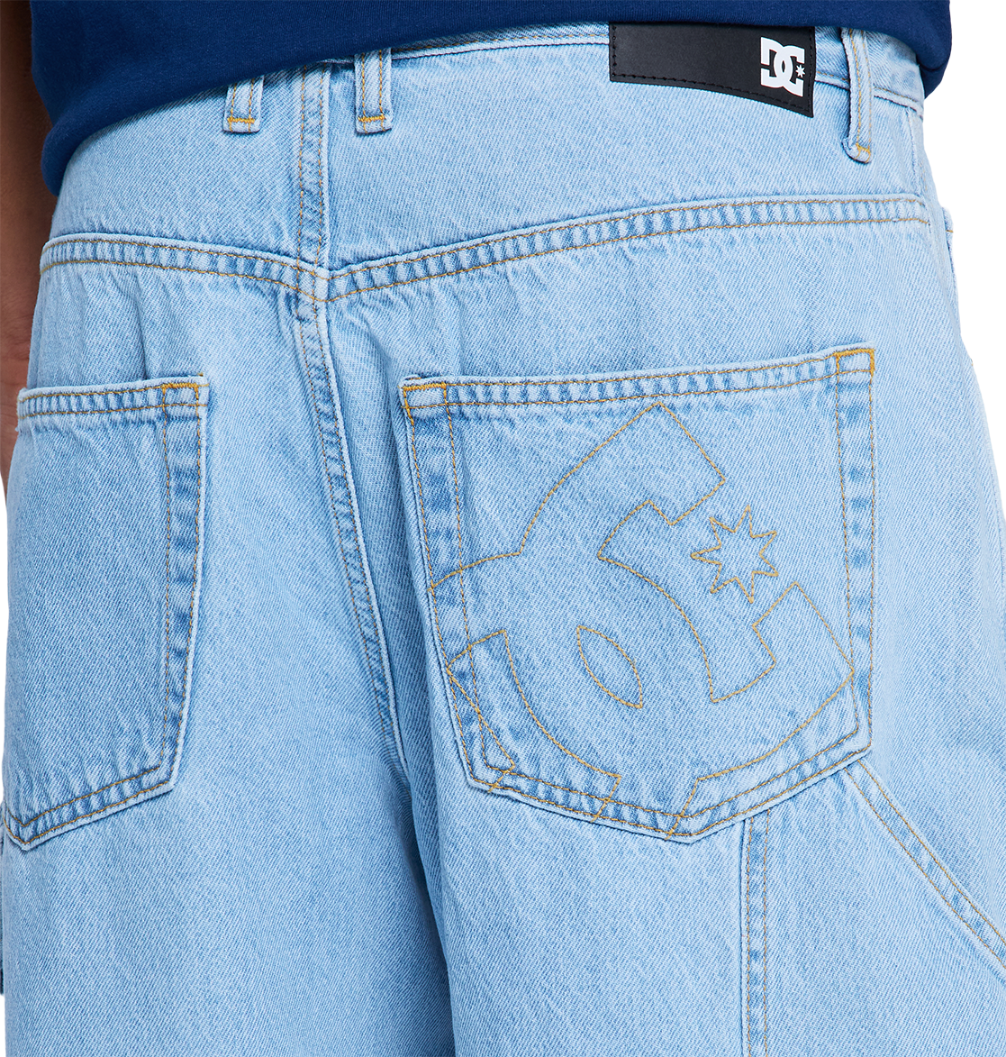 Close-up of DC Shoes Men's Baggy Denim Carpenter Pant in light blue heavyweight denim, featuring a large stitched DC Shoes logo on the back pocket, black label on waistband, and a bold wide-leg fit.