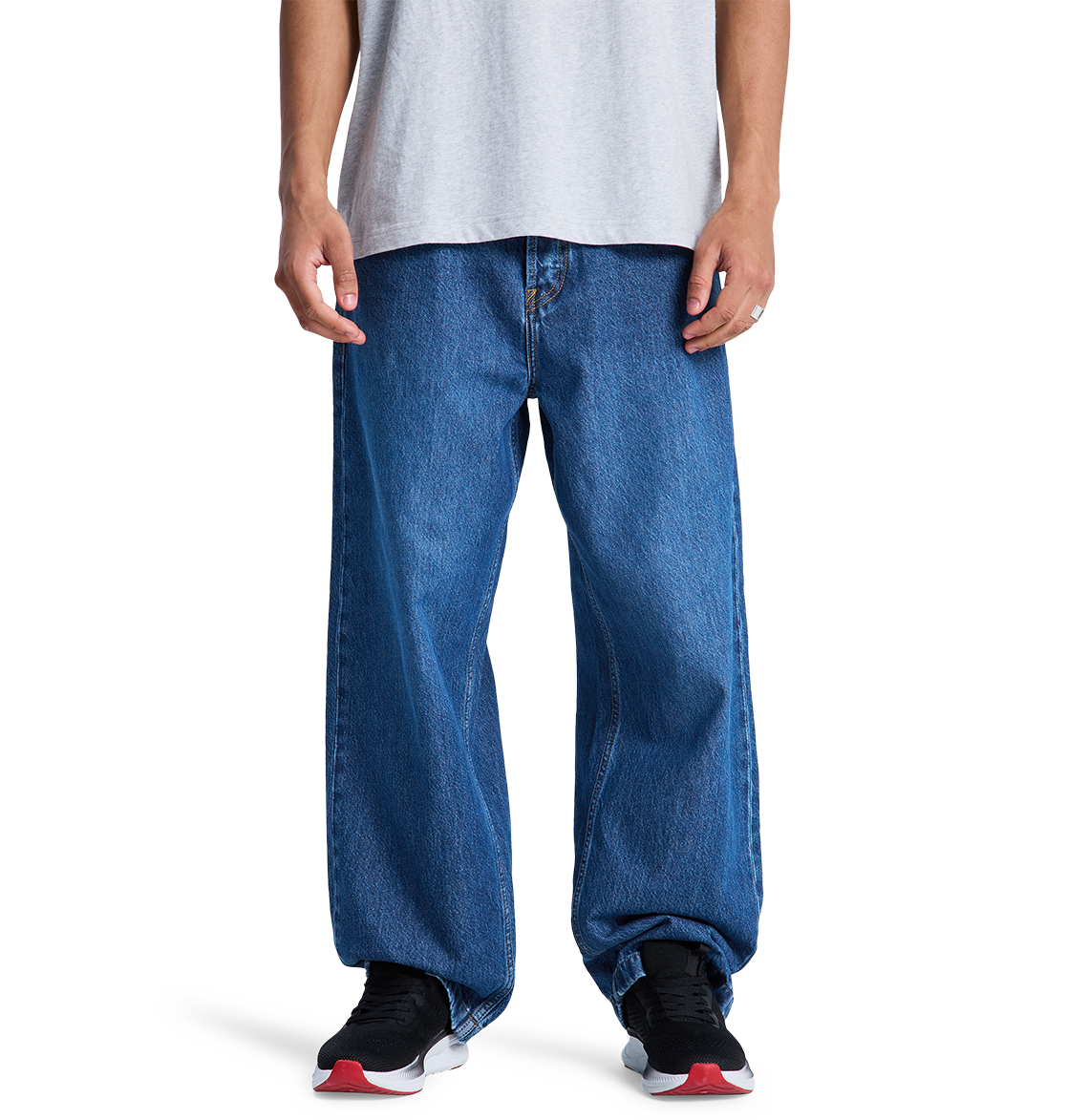 A person wearing DC Shoes' Men's Baggy Denim Pant and black DC sneakers with white soles and red accents stands against a plain white background, paired with a light gray t-shirt.