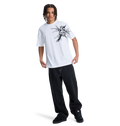 A person with braided hair wears a white graphic tee, black DC Shoes sneakers, and the Men's Baggy Denim Pant by DC Shoes, all set against a plain white background.