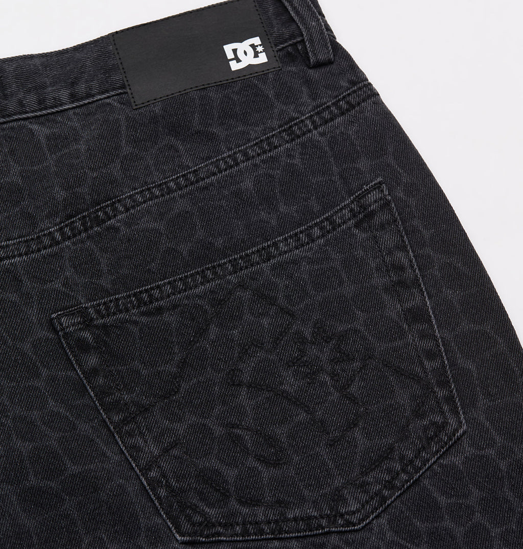 Close-up of the Men's Baggy Denim Snake Print Pant by DC Shoes, showing the black snake print pattern on the back pocket and a small black and white DC Shoes logo tag near the waistband.