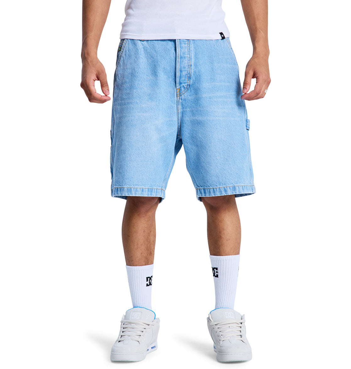 A person wearing Reebok Baggy Denim Carpenter Shorts, a white t-shirt, white socks with black logos, and white sneakers stands against a white background. The photo captures the outfit from the waist down.