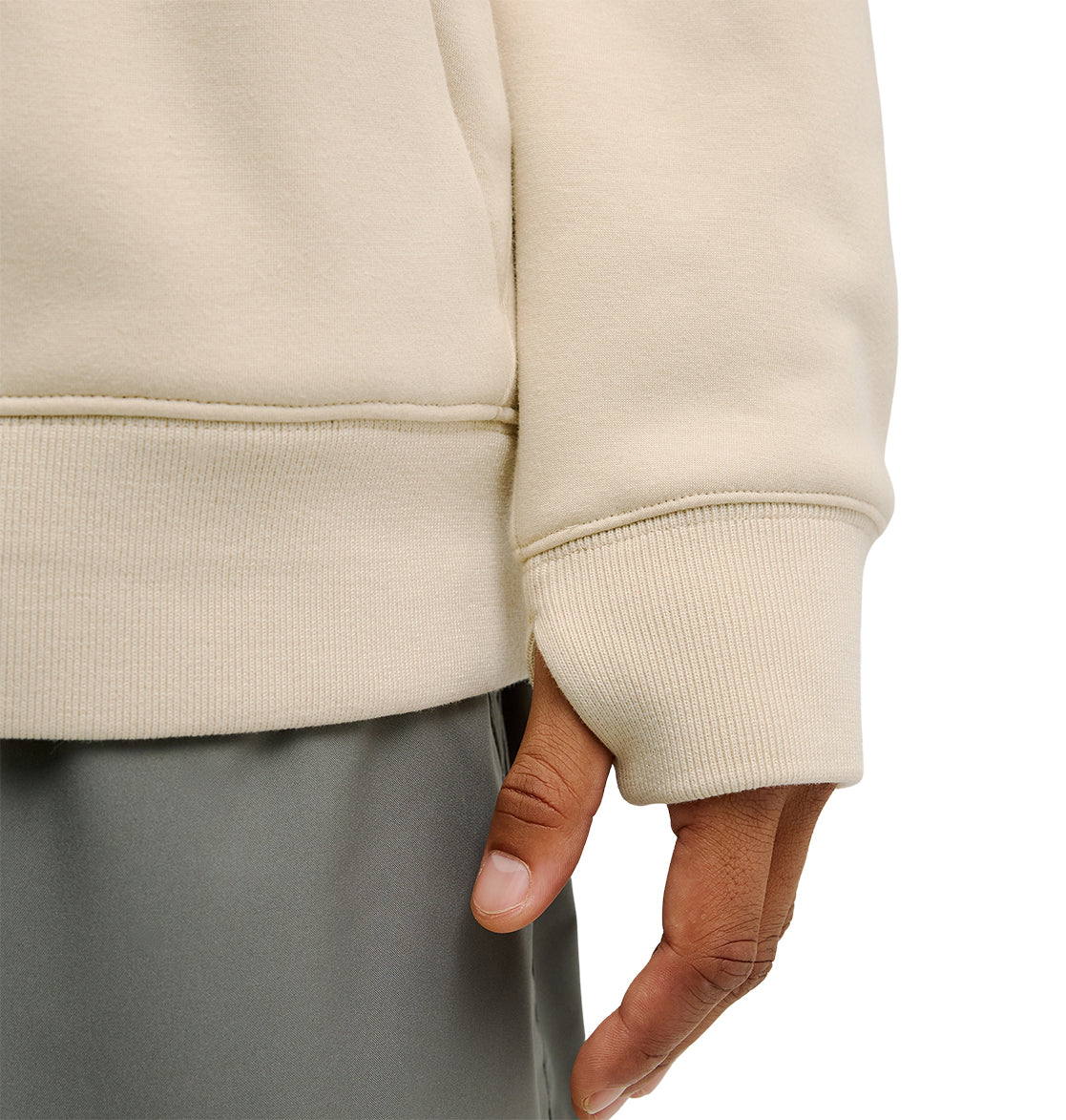 A close-up of a person wearing the DC Shoes Snowstar cream-colored sweatshirt with ribbed cuffs and hem, designed for a comfortable fit, paired with gray pants. Only the person’s right hand and part of their torso are visible.