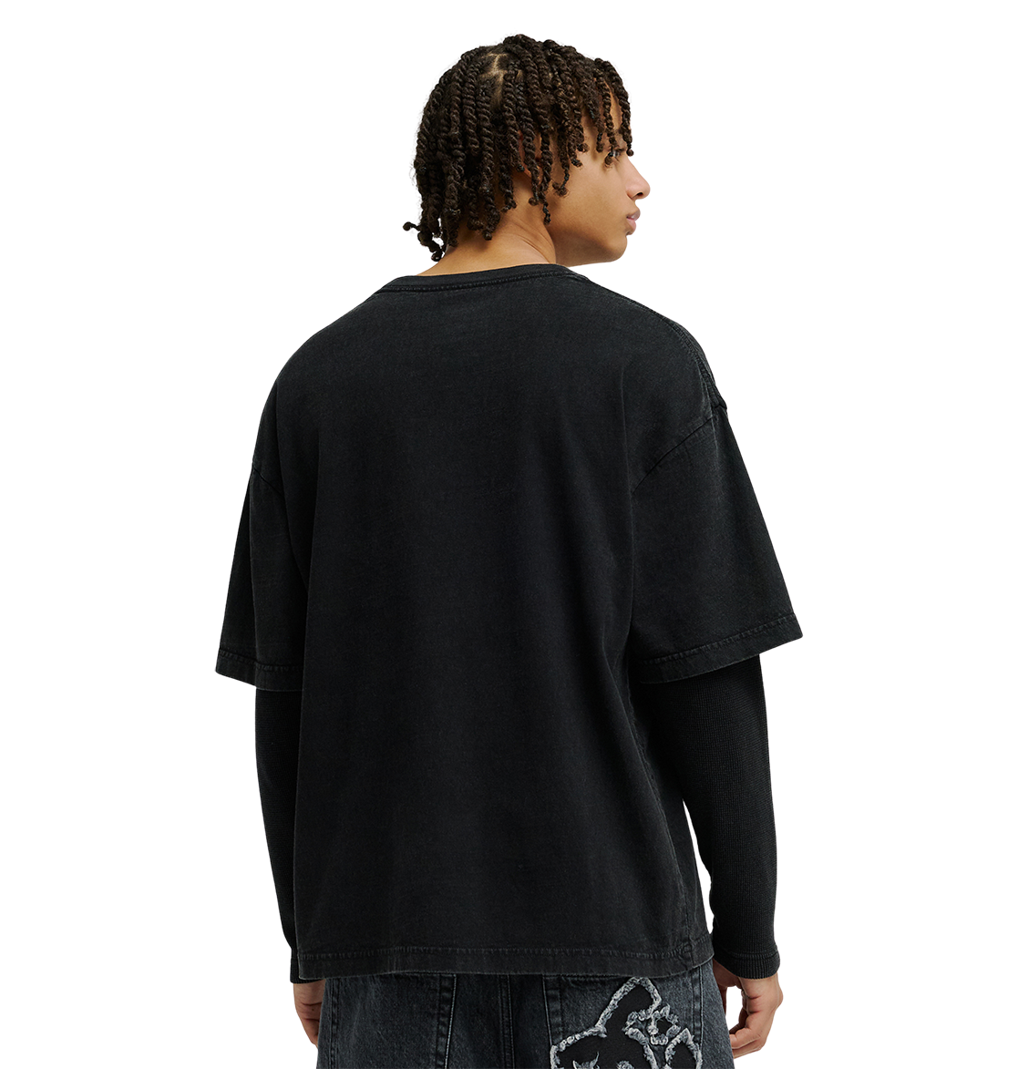 A person with short twists embodies streetwear style, wearing a loose black T-shirt layered over the DC Shoes Men’s DC Twofer Long Sleeve tee and black jeans with a white graphic, standing and facing away.
