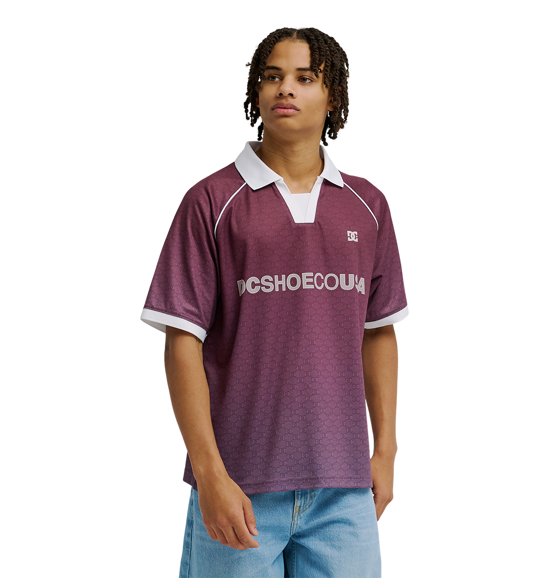 A young man models the Men's DC Soccer Top by DC Shoes, featuring maroon fabric with white trim, paired with light blue jeans against a plain white background for an athletic, casual look.