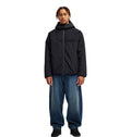 A person wearing the DC Shoes Coldstag Sherpa Reversible hooded jacket in black, paired with loose blue jeans and black shoes, stands facing forward against a plain white background.