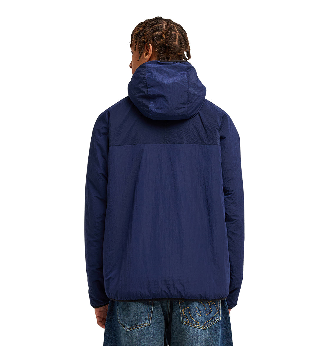 A person with braided hair, seen from behind, wears the DC Shoes Coldstag Sherpa Reversible jacket in dark blue for cold-weather comfort and loose-fitting blue jeans. The background is plain white.