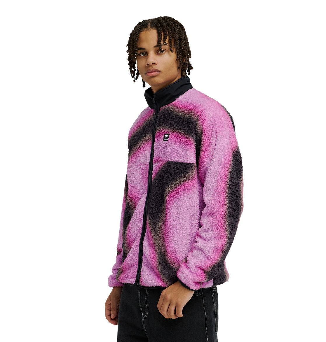 A person with braided hair wears the DC Shoes Lynx Fleece—a soft, fuzzy pink and black zip-up jacket with a black collar—paired with black pants, standing against a plain white background.