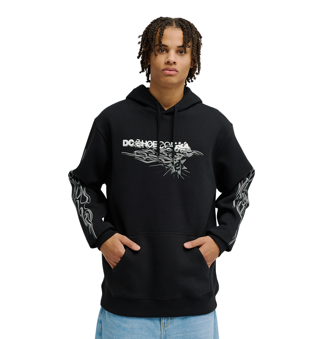 A person wearing the Men's Side Flame Hoodie from DC Shoes—a black pullover featuring bold white DC graphics on the front and sleeves—stands with hands in the spacious front pocket against a simple, light backdrop. The hoodie’s fleece construction delivers cozy warmth and stylish comfort to the overall look.