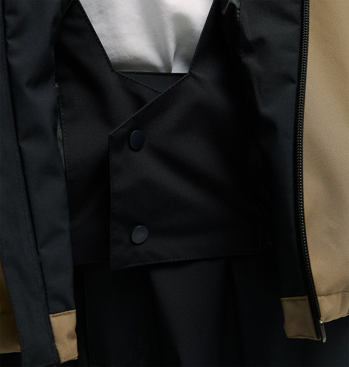 Close-up of a black double-breasted vest with two buttons, layered over a white shirt and underneath the DC Shoes Edge Jacket 20K, a tan and black venting ski jacket with a zipper.
