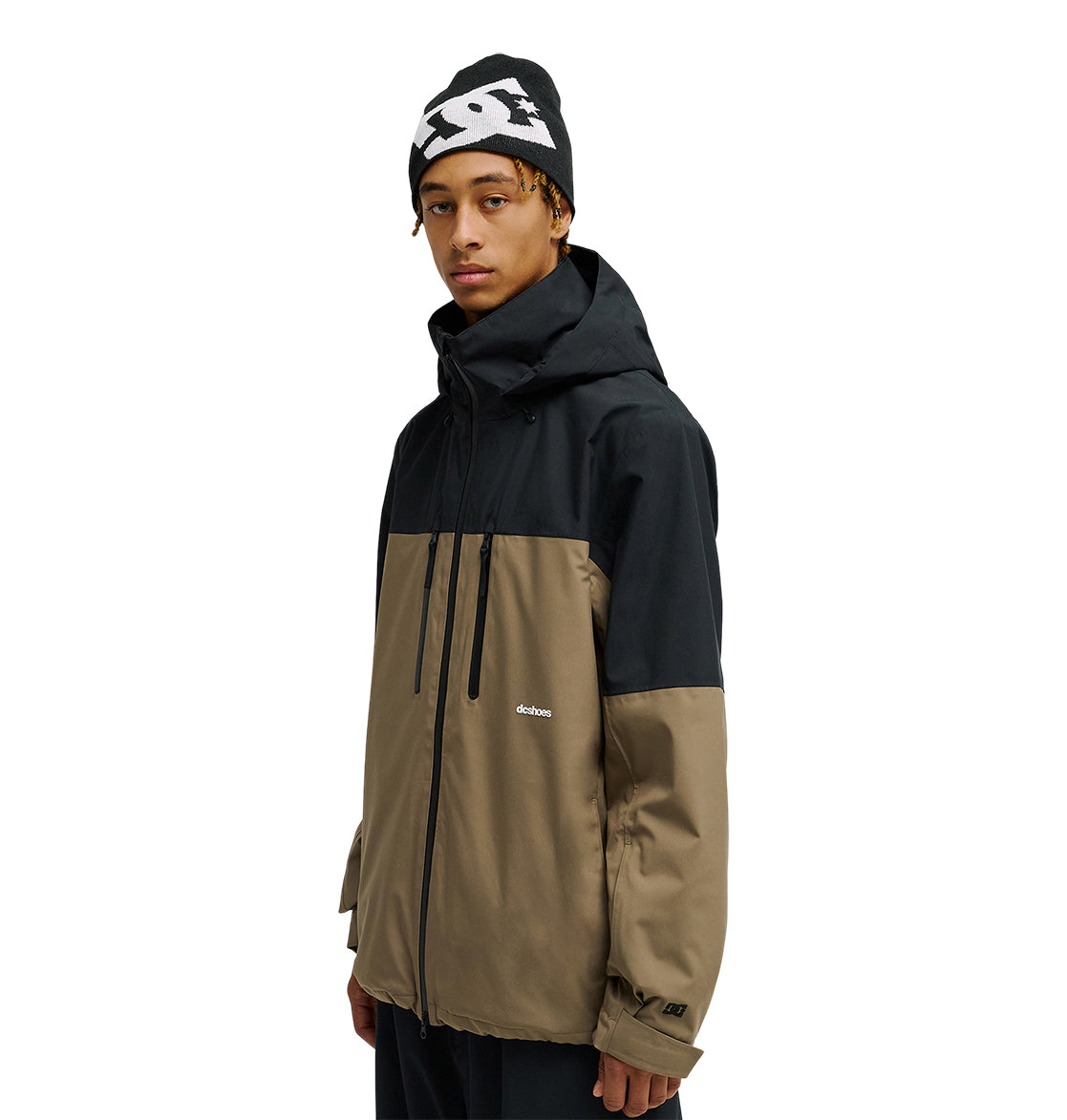 A person wearing the DC Shoes Edge Jacket 20K in black and tan, featuring “dcshoes” on the chest, along with a black beanie with a white pattern, standing against a white background.