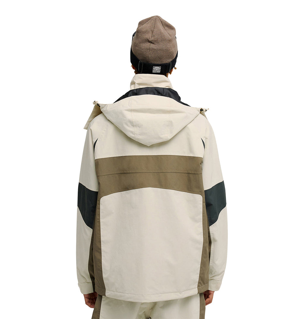 A person is seen from the back wearing the DC Shoes Mountain Lab Jacket 20K—a hooded, color-blocked jacket in beige, brown, and black designed for breathable protection. They also sport a brown beanie and light-colored pants while standing against a plain white background.
