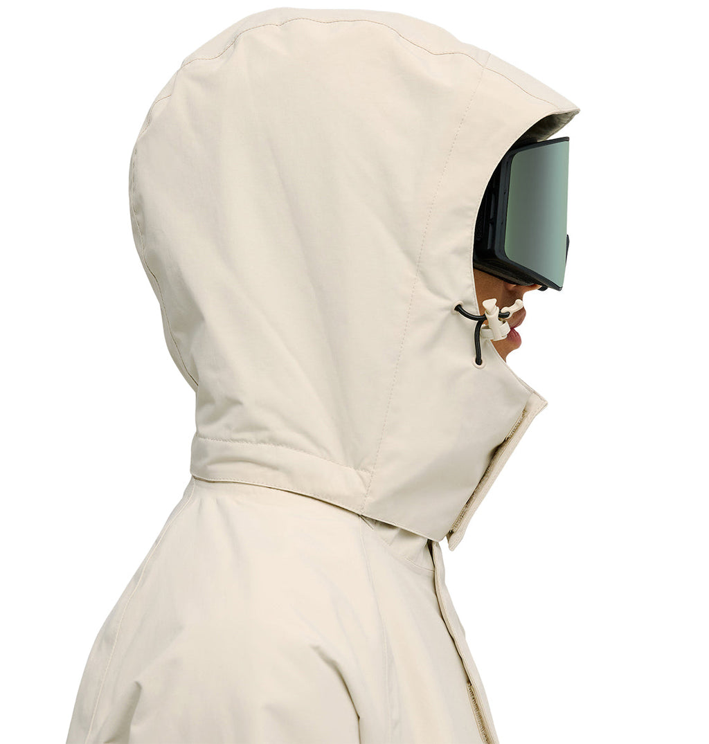 A person in the DC Shoes Mountain Lab Jacket 20K—a beige hooded jacket designed for breathable protection—paired with large ski goggles, shown in profile facing right against a white background.